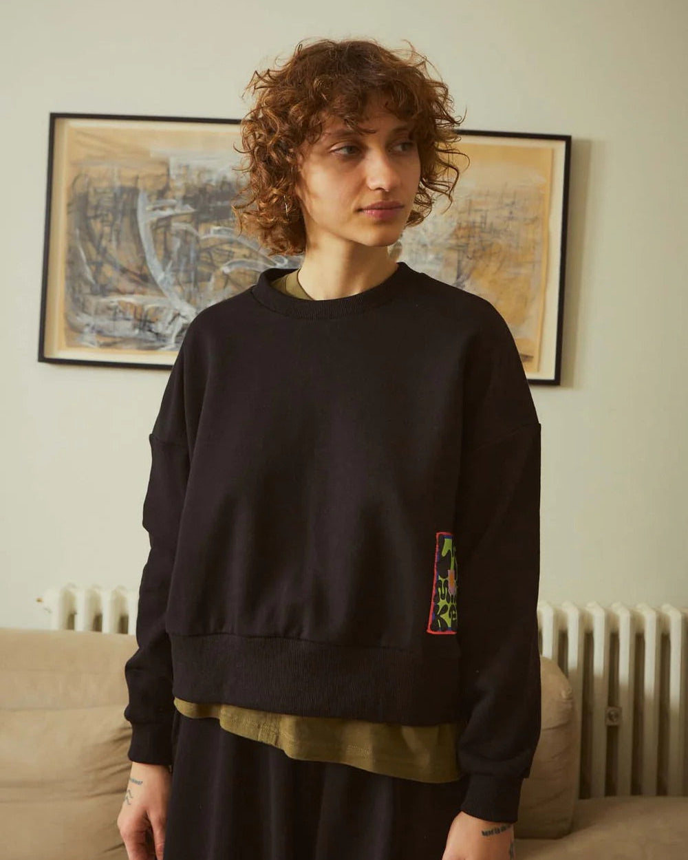 Person wearing a black sweater with a colorful patch in a room with a map on the wall.