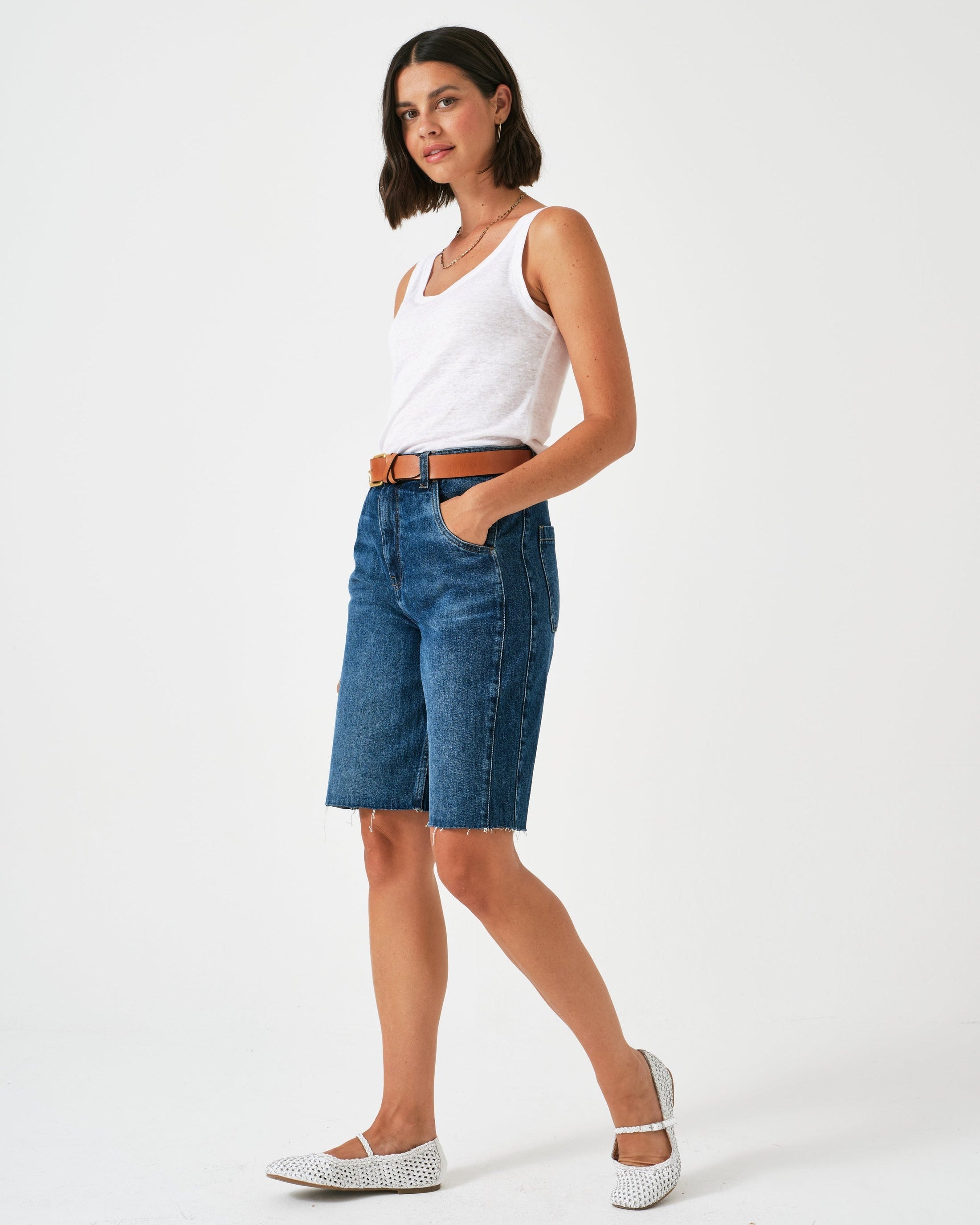 Woman wearing a white tank top and blue denim shorts on a white background