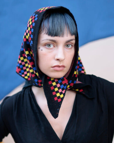 Person wearing a colorful checkered headscarf against a blue background