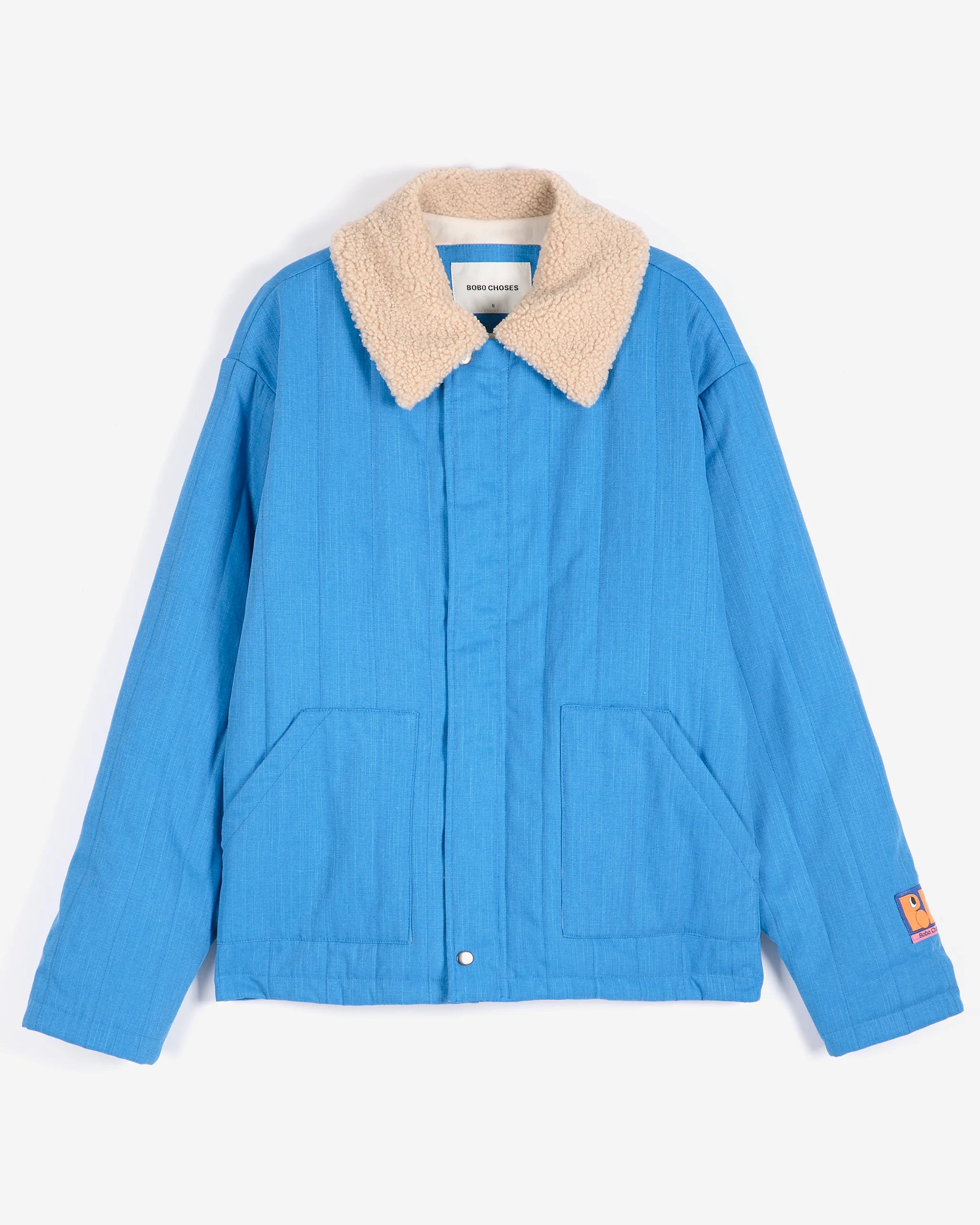 A blue quilted jacket with a beige sherpa collar, featuring front patch pockets and a small orange label on the left sleeve, displayed against a clean white background.