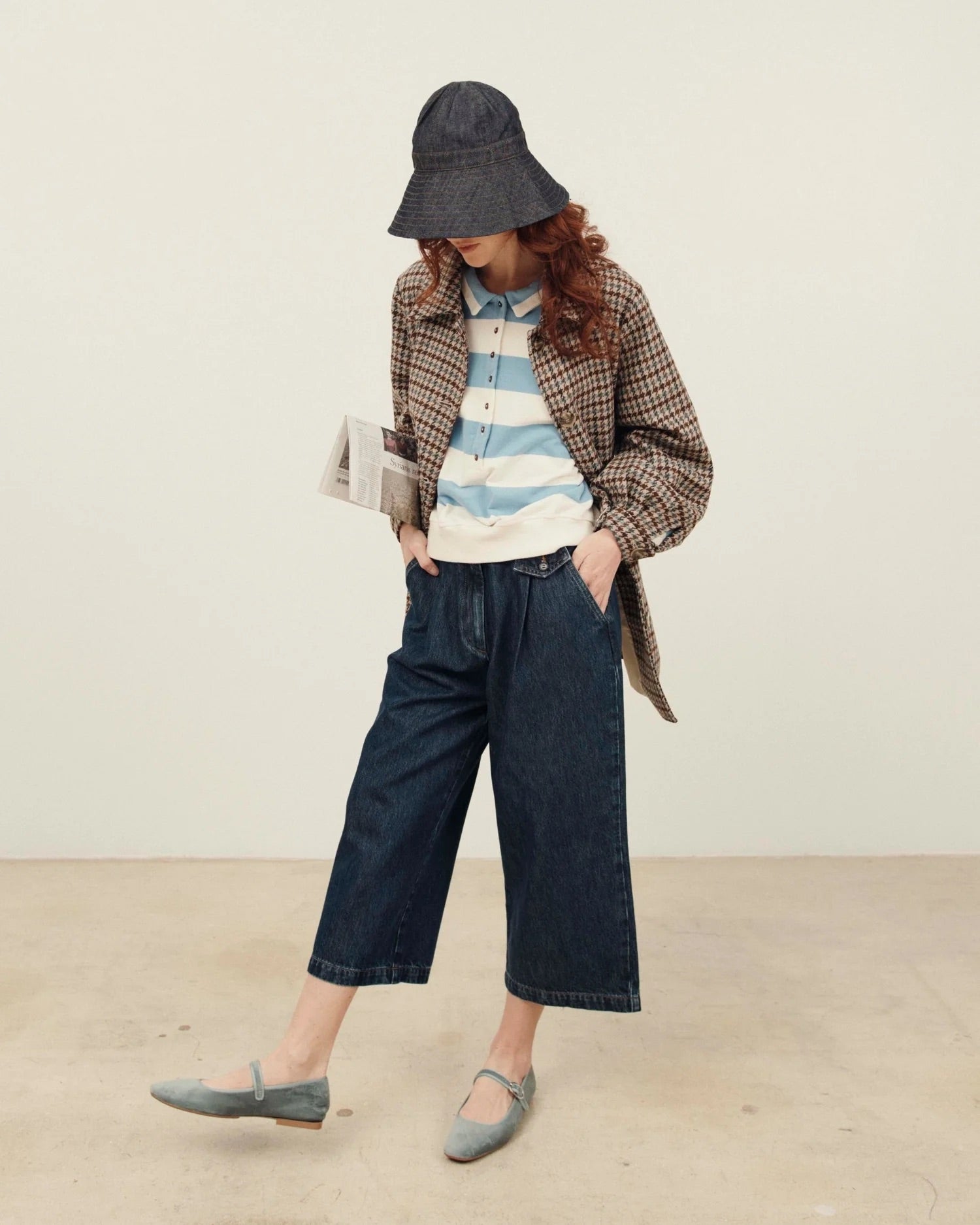 Person wearing a plaid coat, striped shirt, and wide-leg jeans with a hat on a plain background