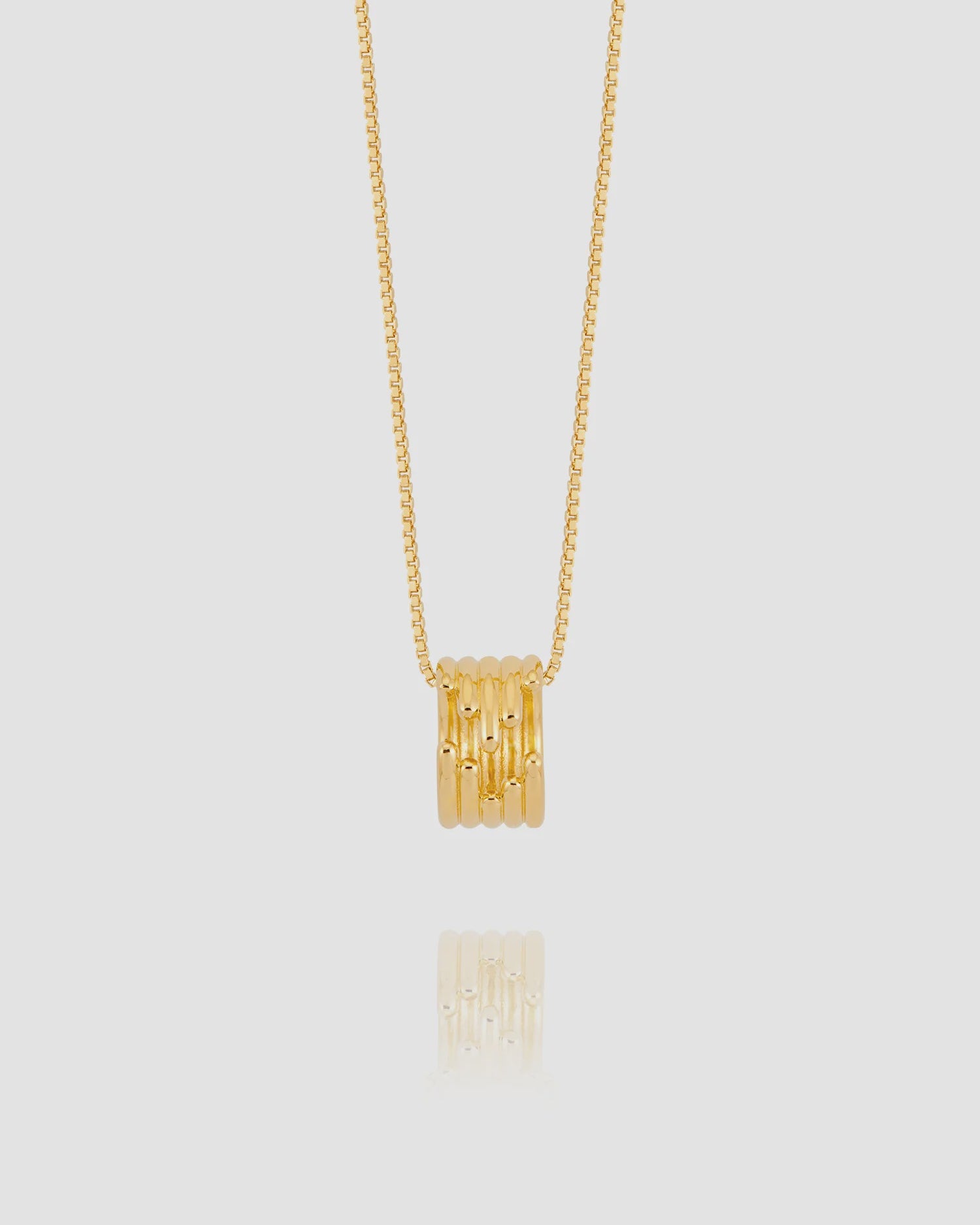Gold necklace with a cylindrical pendant on a light gray background