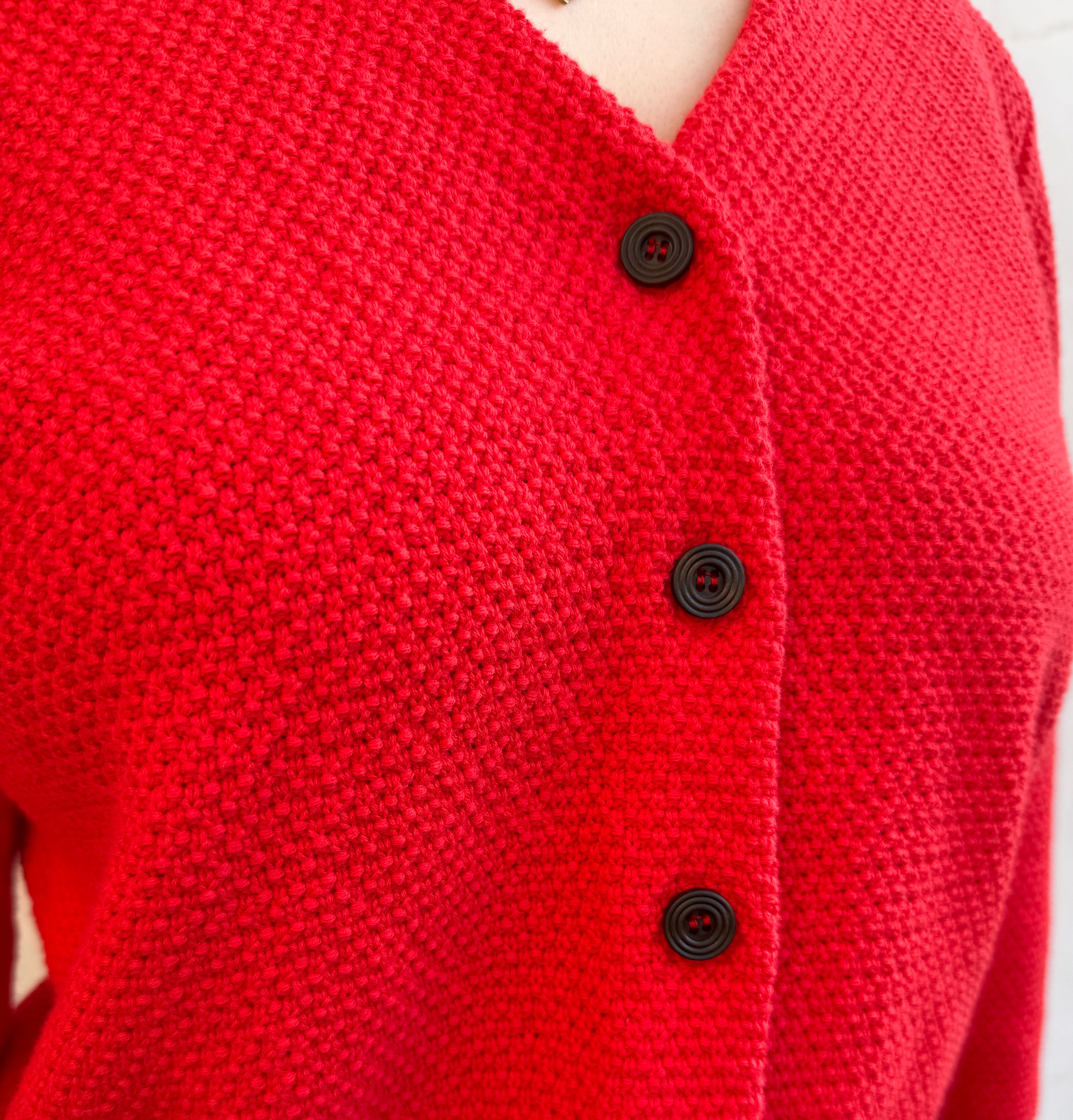 Close-up of a red knitted cardigan with brown buttons on a blurred background
