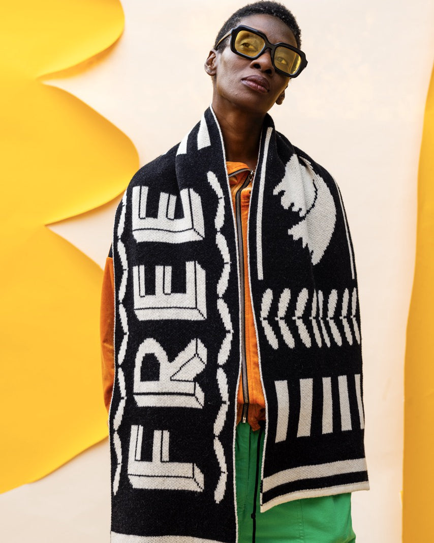 Person wearing a black and white patterned scarf with 'FREE' text, standing against a yellow and beige background.