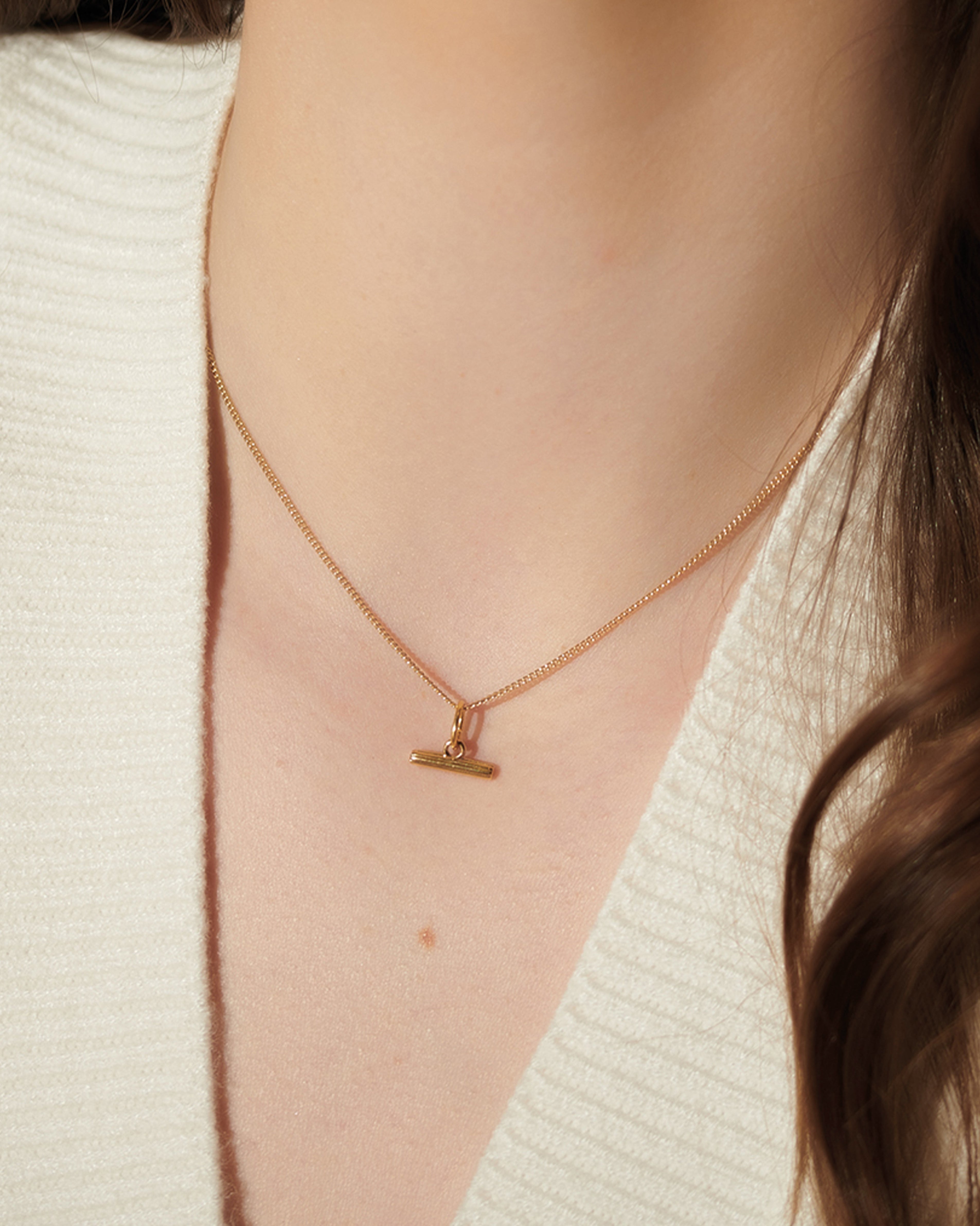 Gold necklace with a small pendant worn by a person against a neutral background