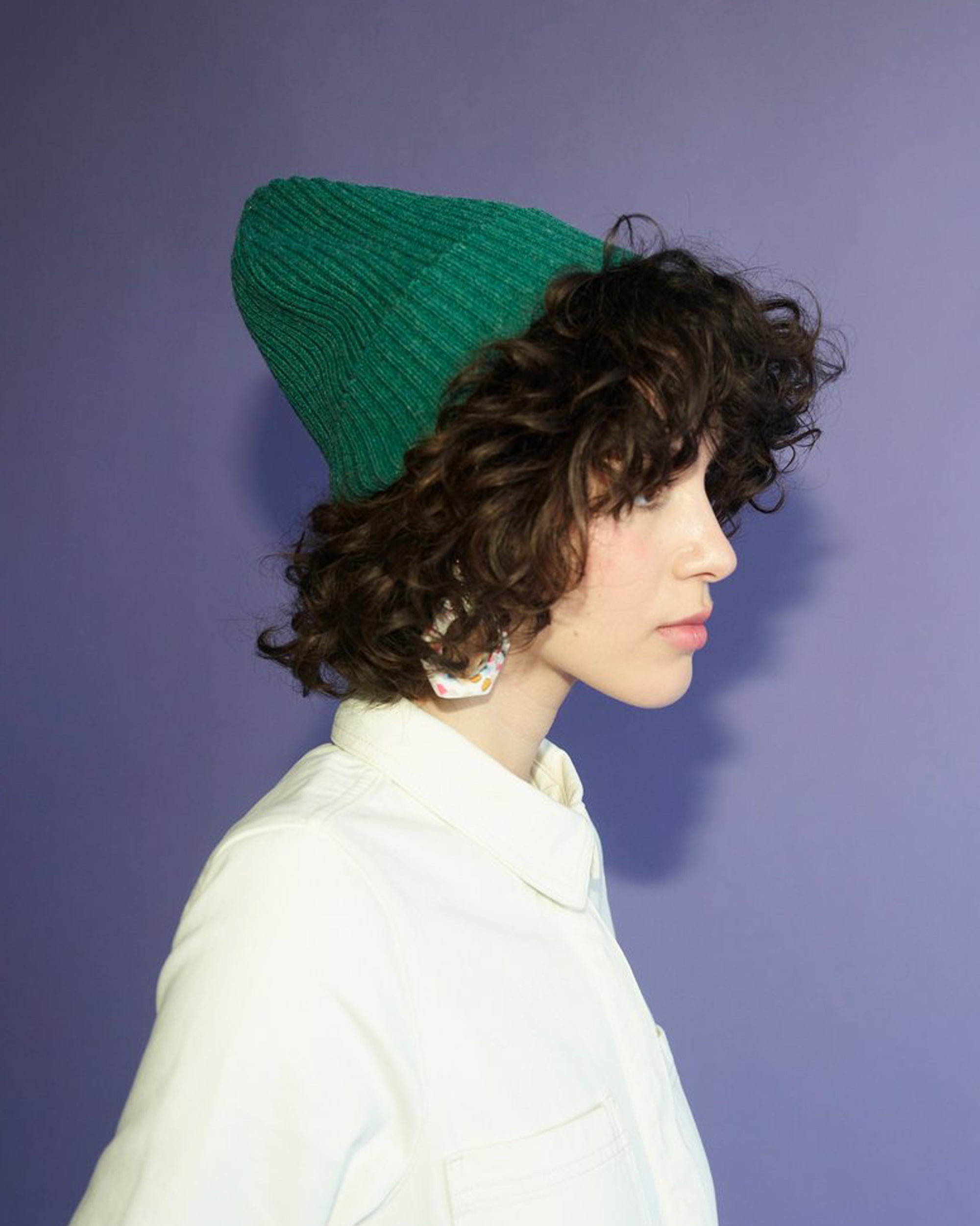 Person wearing a green knitted beanie against a purple background.