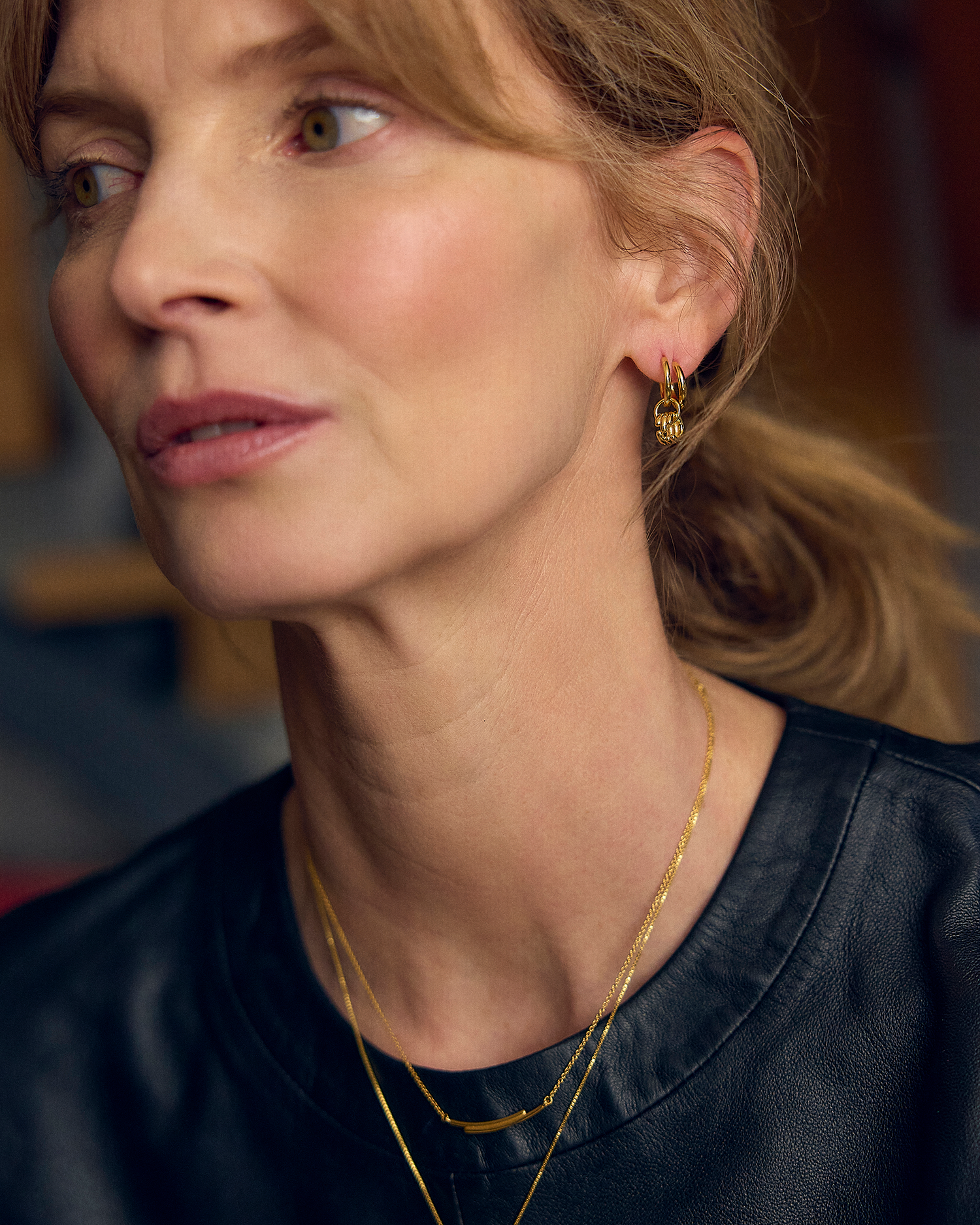 Close-up of a woman wearing gold earrings and necklaces with a blurred background