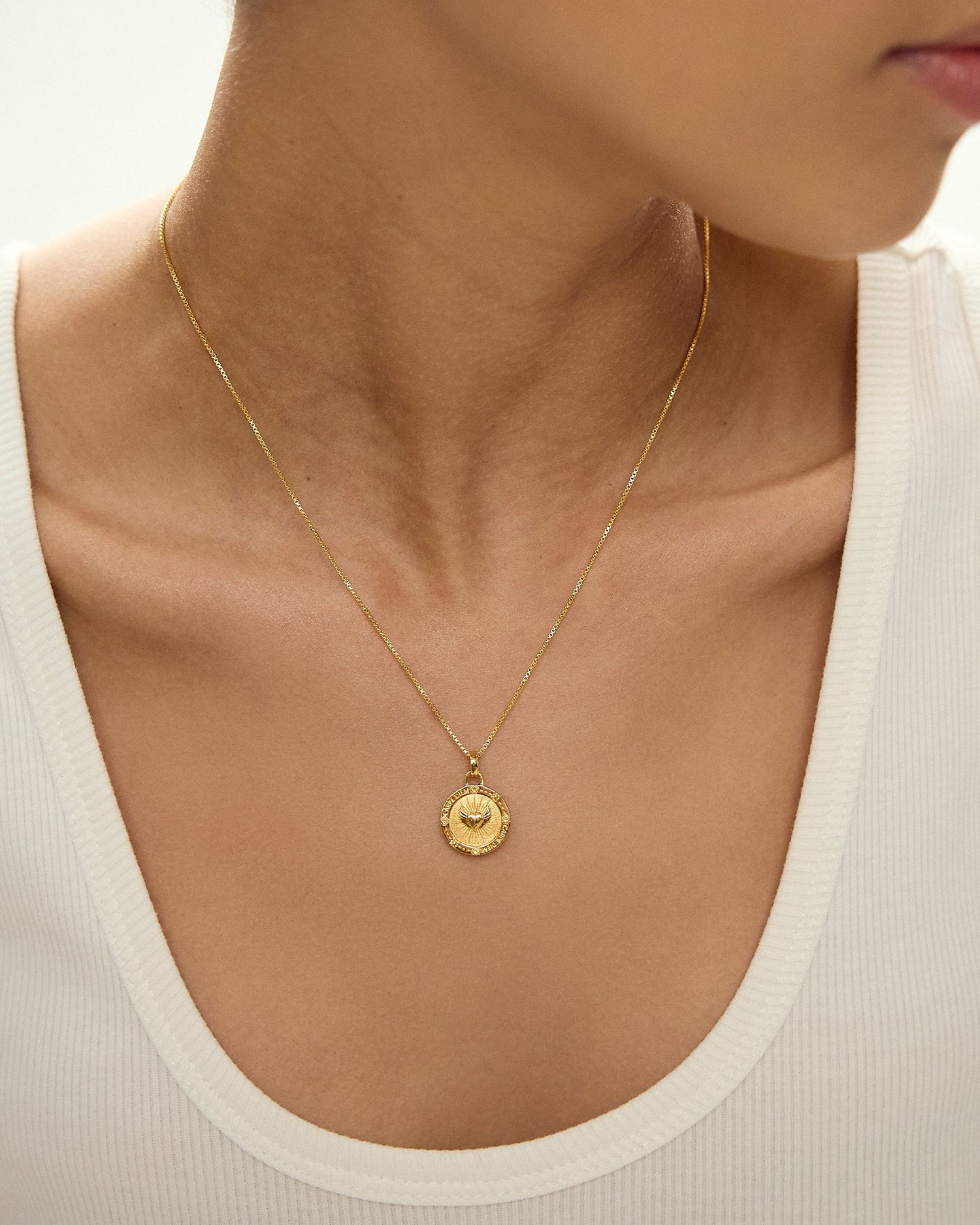Gold necklace with a pendant on a person wearing a white top