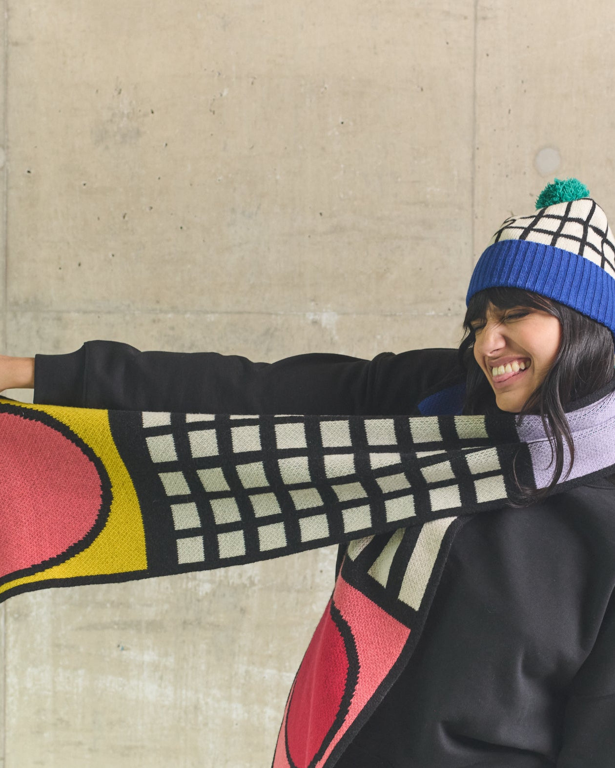 Person wearing a colorful scarf and beanie against a concrete wall
