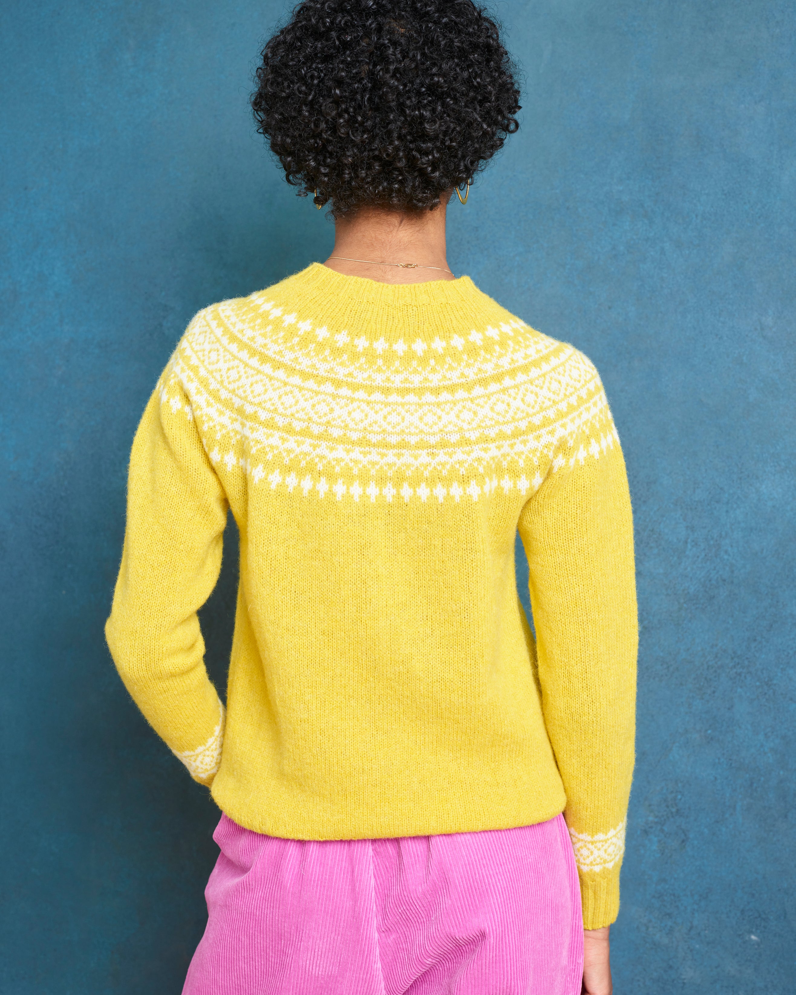 Person wearing a yellow sweater with a patterned neckline against a blue background