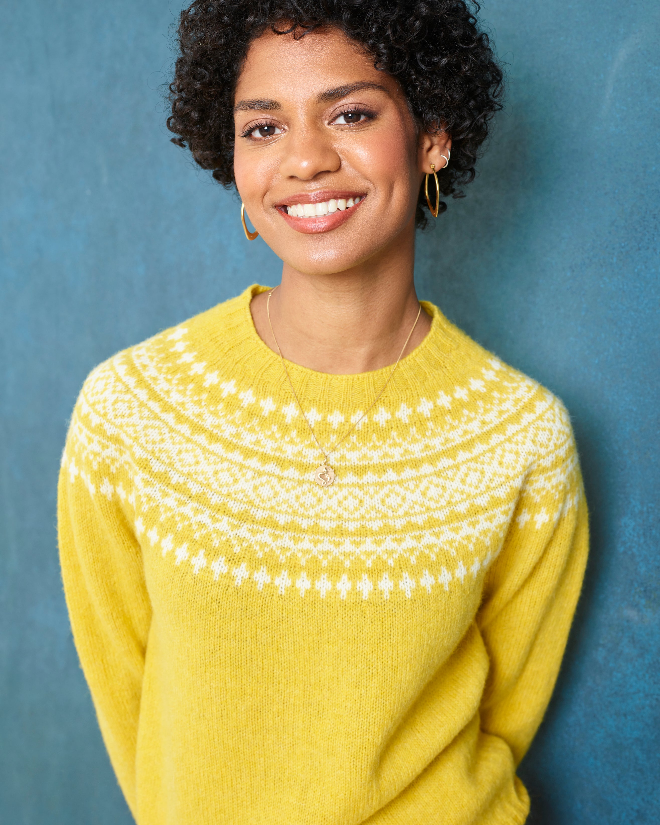 Woman wearing a yellow sweater with white patterns against a blue background