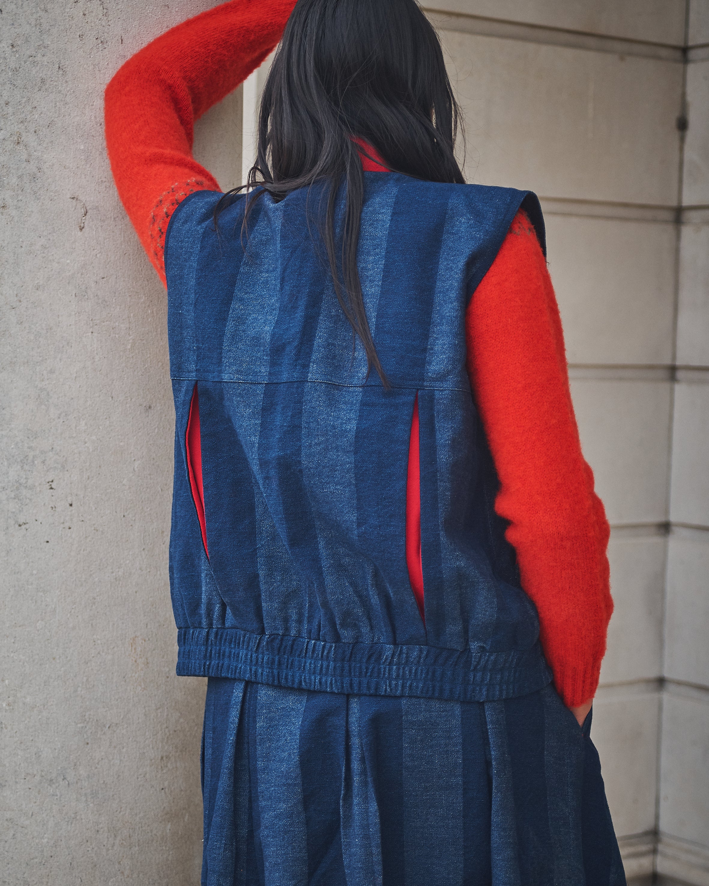 Person wearing Lowie denim stripe gilet against a stone wall.