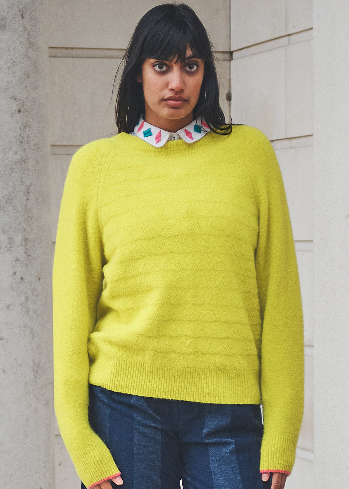 Woman wearing a bright yellow sweater with a patterned collar against a neutral wall.