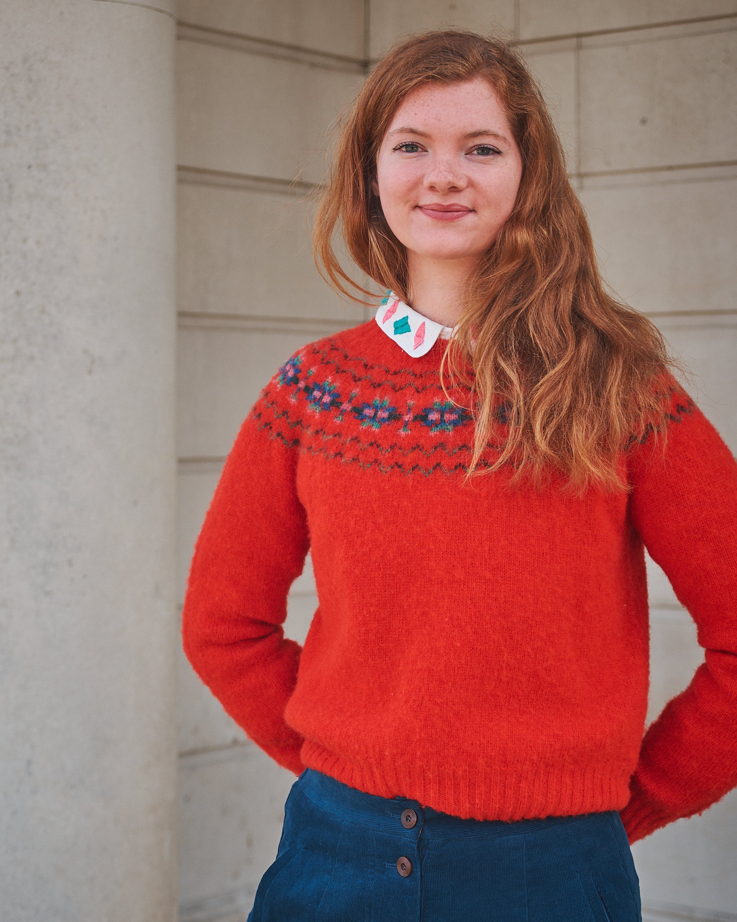 Person wearing a red sweater with a pattern, standing against a light-colored wall.
