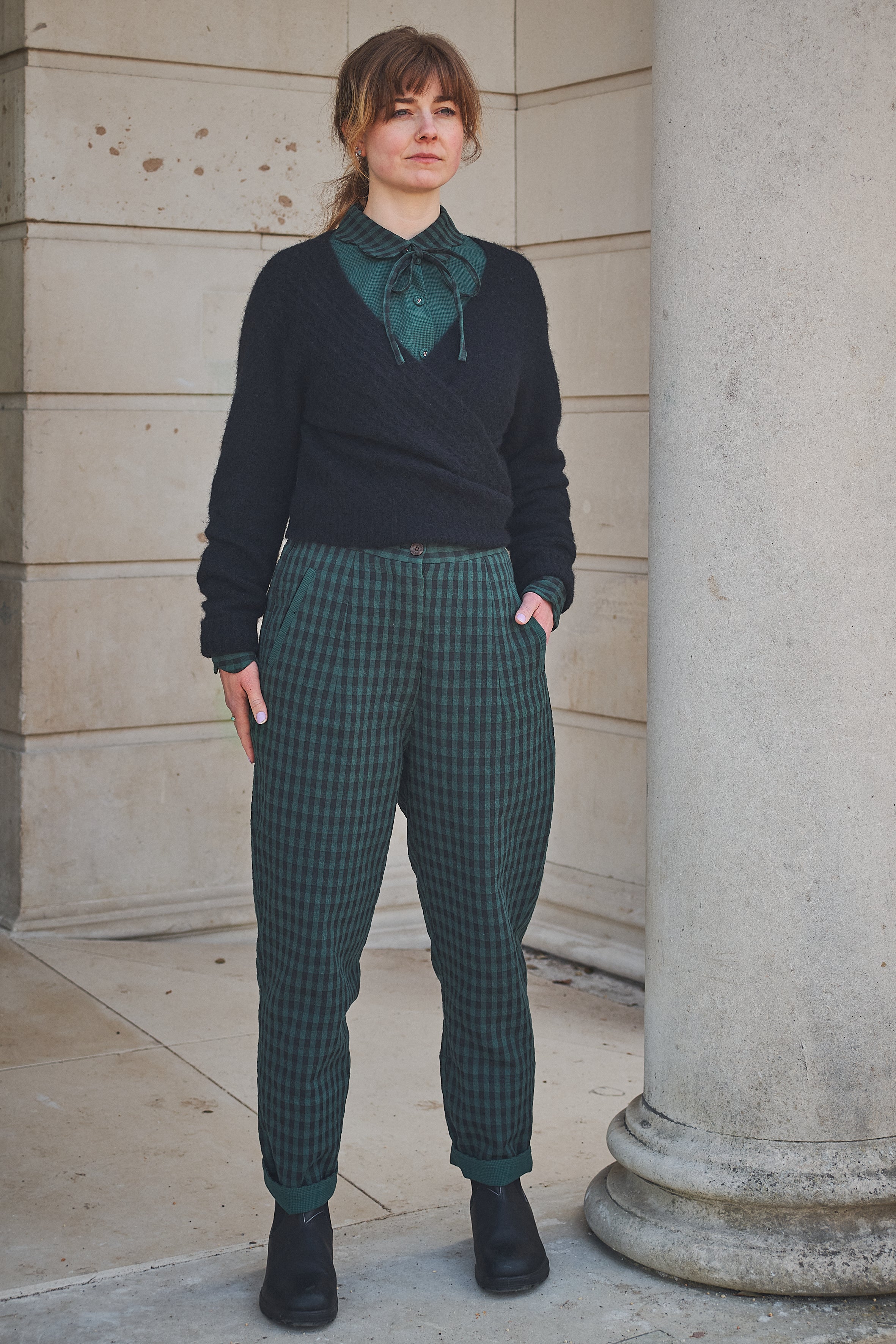 Woman wearing Lowie Green Check Trousers standing against a stone wall.