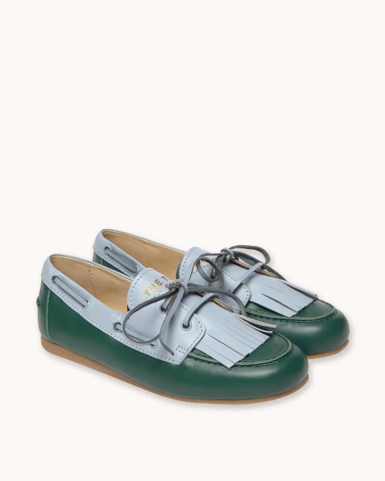 A pair of boat-style loafers in forest green and light blue, featuring fringe detailing and dark gray laces, set against a plain off-white background.
