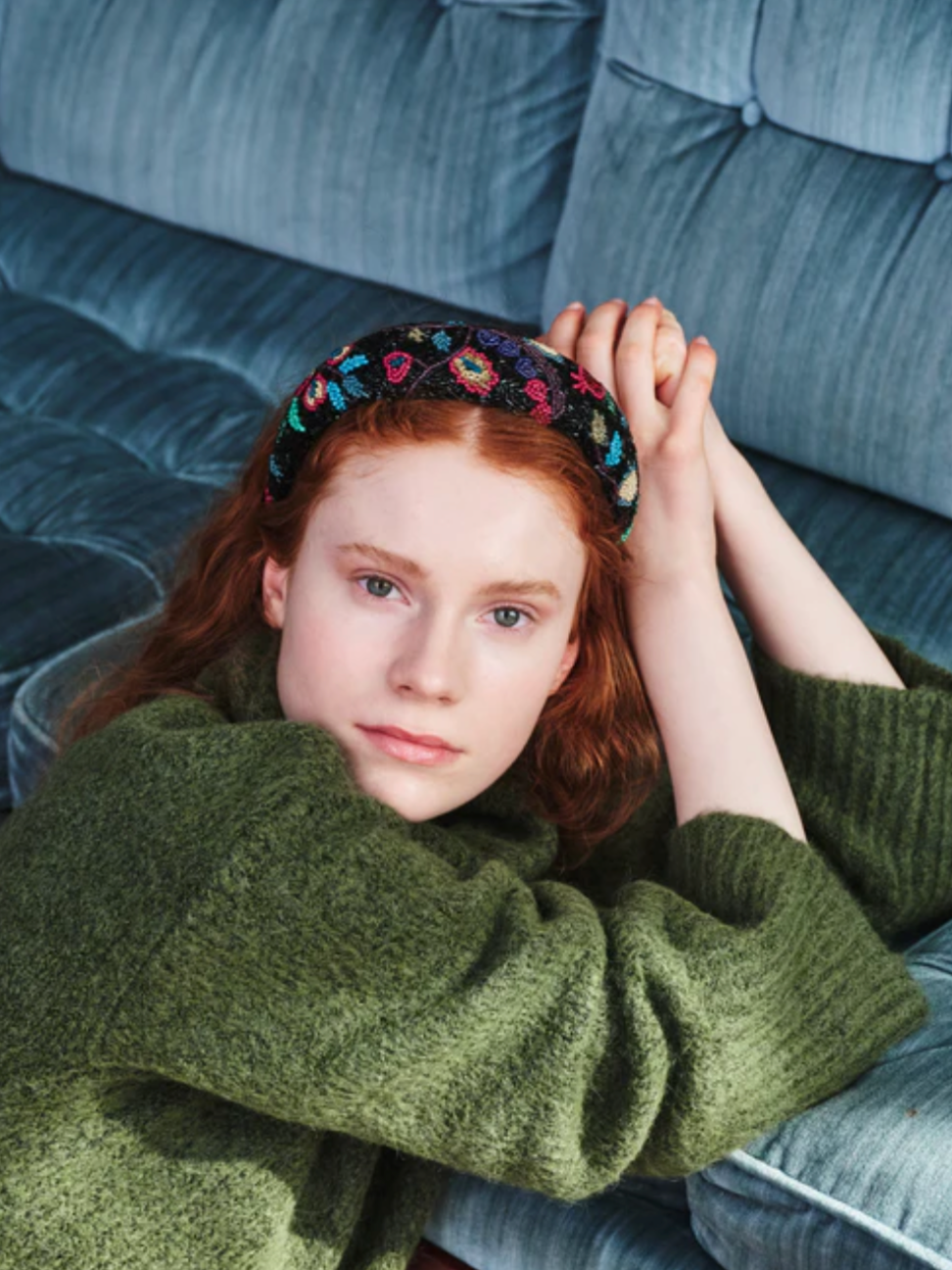 Person wearing a green sweater and floral headband sitting on a blue couch.
