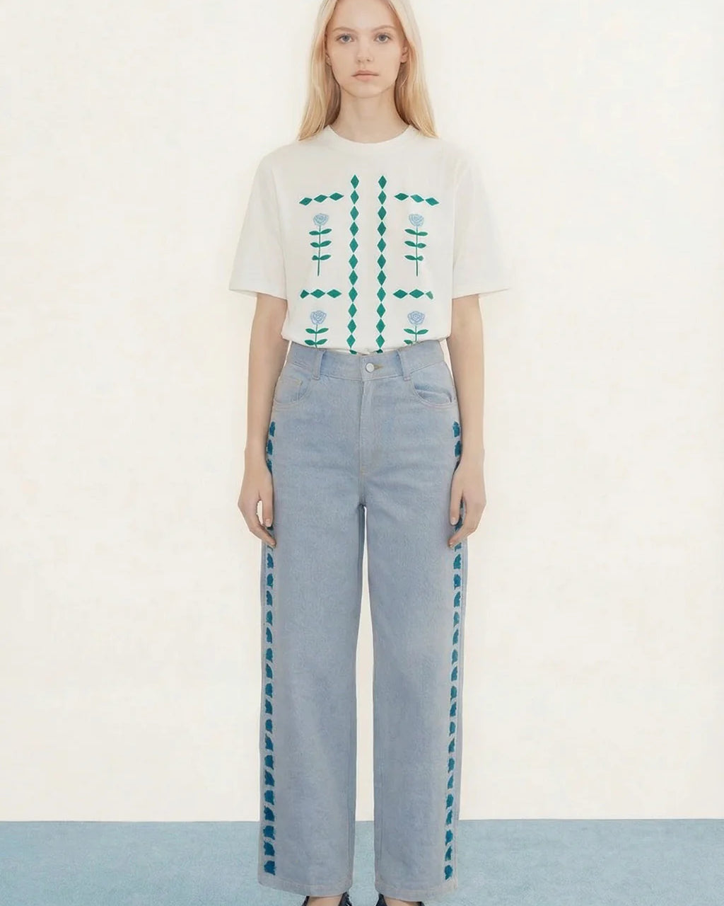 Woman wearing a white floral top and light blue pants on a plain background