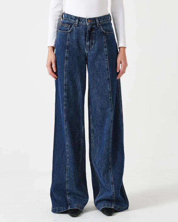 Woman wearing a white long-sleeve top and blue wide-leg jeans on a white background