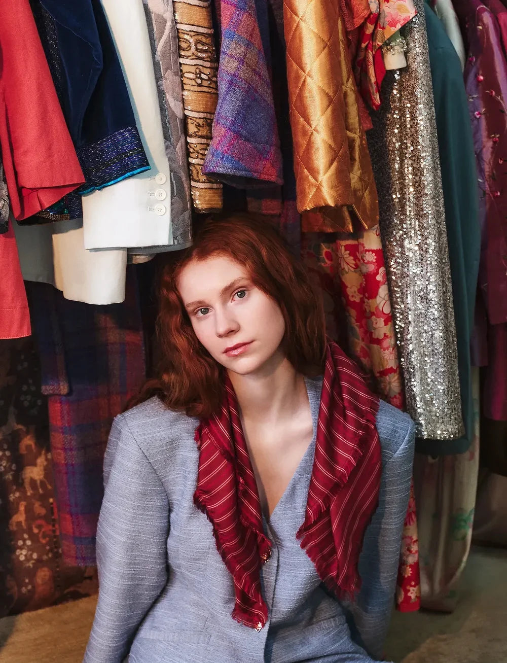 Woman with red hair sitting in front of a rack of colorful clothing