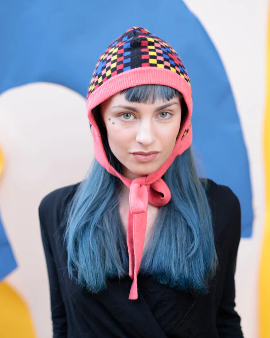 Person wearing a colorful helmet with a pink chin strap against a multicolored background