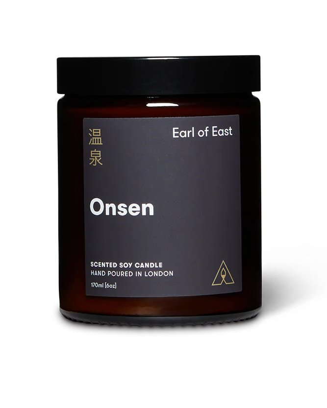 A hand-poured soy wax candle in an amber glass jar with a black label reading 'EARL OF EAST ONSEN'