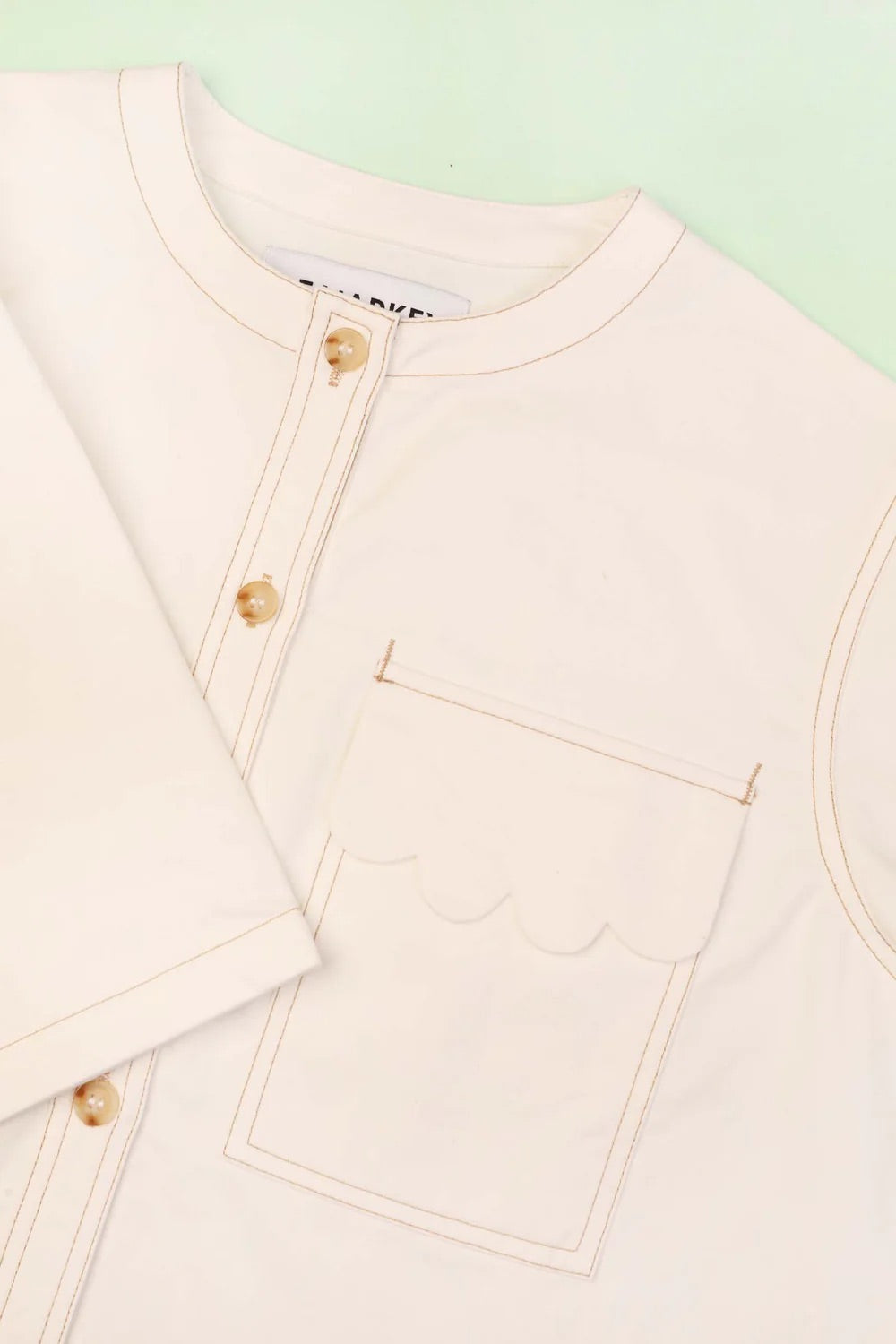 Close-up of a light pink jacket with gold buttons on a light green background