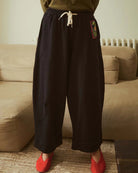 Person wearing black wide-leg pants with a patch, standing in a living room.