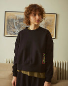 Person wearing a black sweater with a colorful patch in a room with a map on the wall.