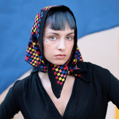 Person wearing a colorful checkered headscarf against a blue background