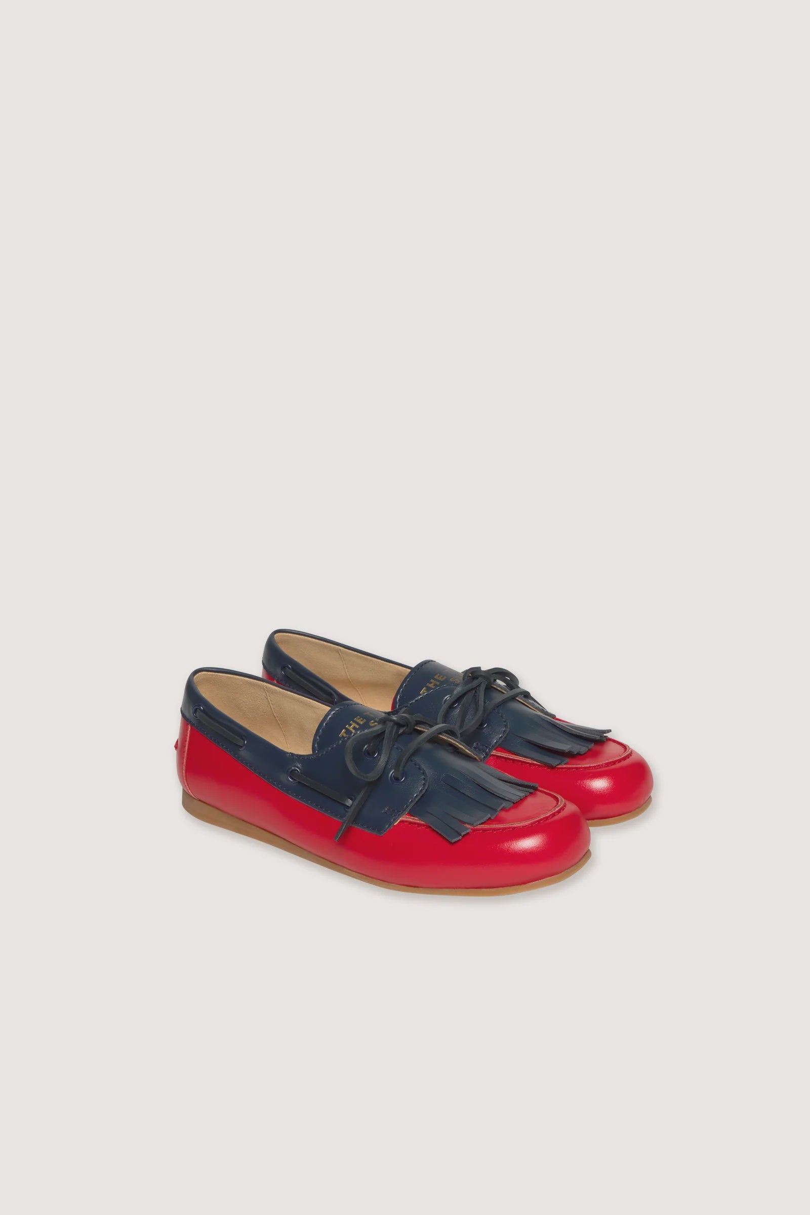 A pair of children's boat-style loafers in navy blue and bright red, shown on a light beige background.