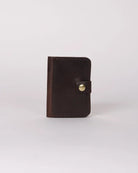 A small dark brown leather card holder or wallet with a snap button closure, standing upright on a light gray background.