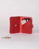 A small red leather bifold wallet shown open on a light gray studio background, with card slots holding cards and a coin placed nearby.