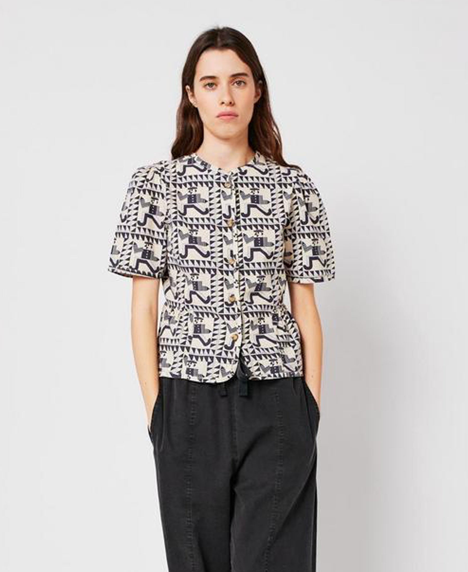 Woman wearing a patterned shirt and dark pants on a plain background