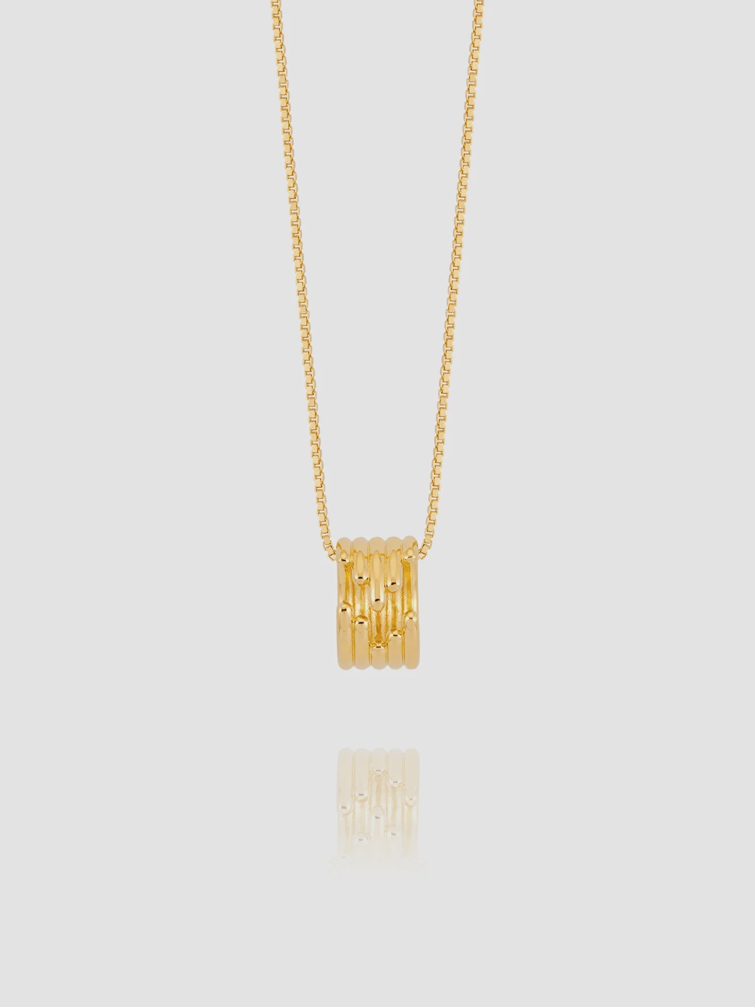Gold necklace with a cylindrical pendant on a light gray background