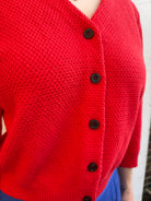 Close-up of a red knitted cardigan with brown buttons on a blurred background