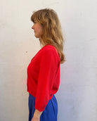 Person wearing a red sweater and blue pants on a white surface with a brick background