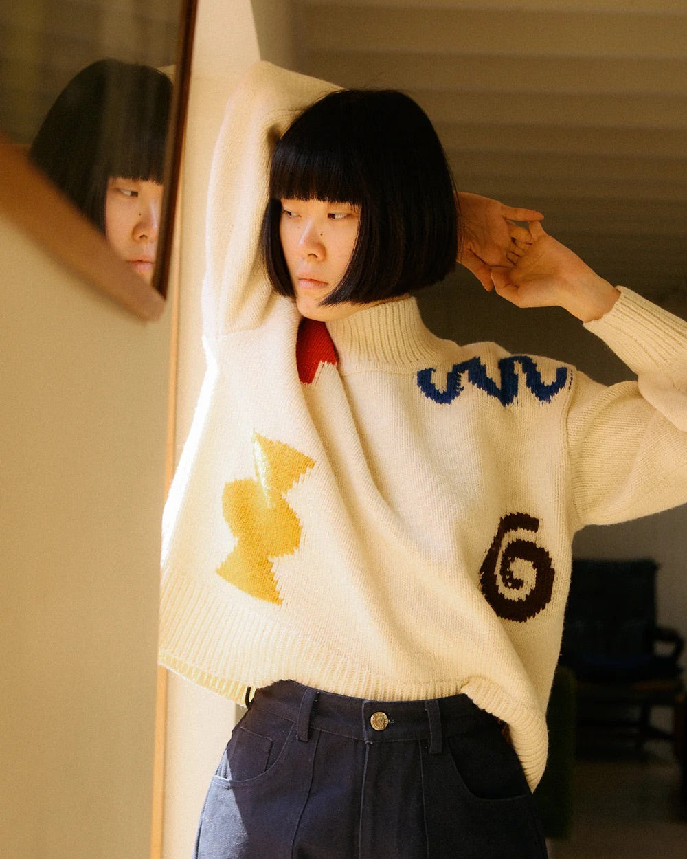 Person wearing a white sweater with colorful designs, standing in front of a mirror.