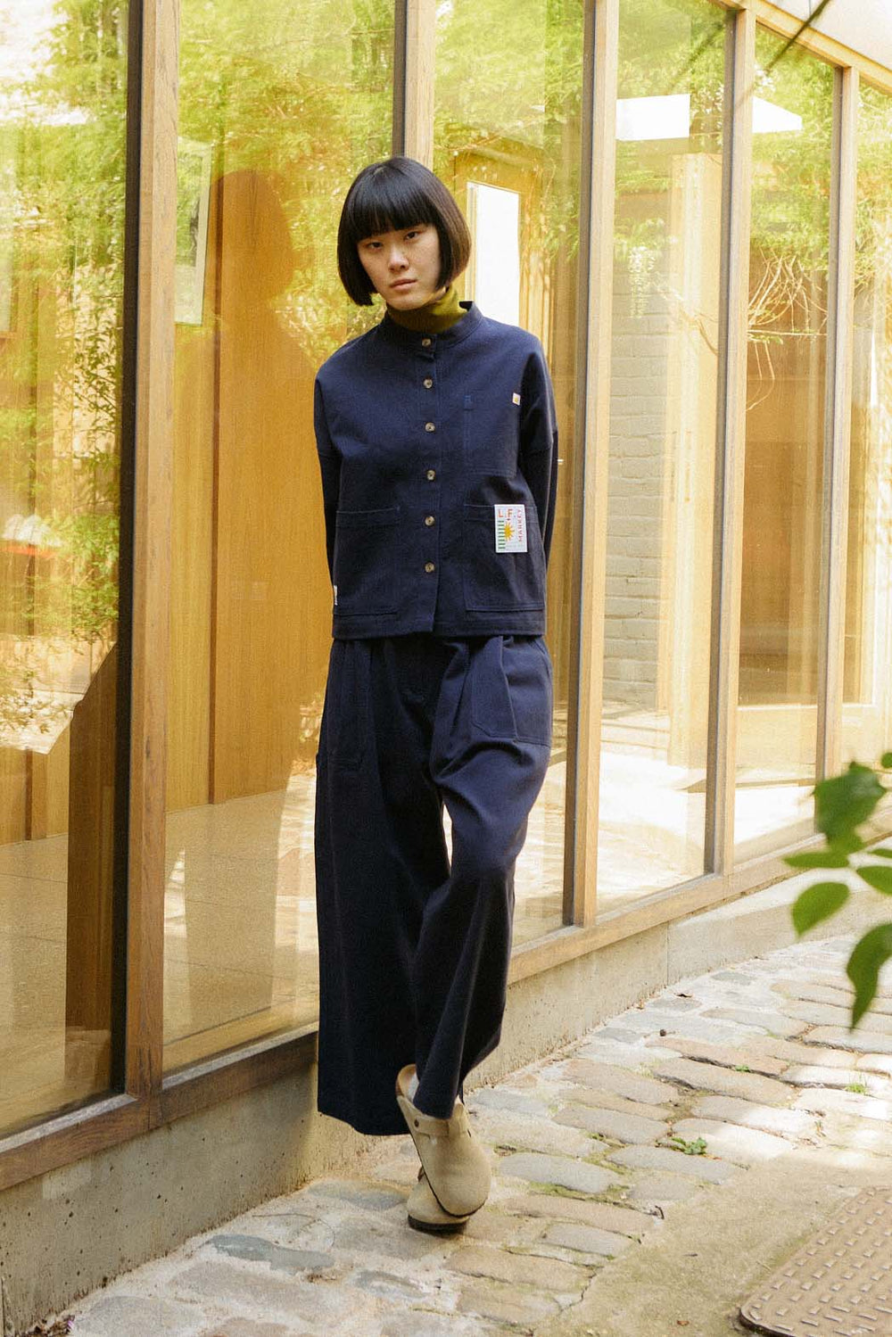 Person wearing a navy blue outfit standing in front of a glass building.