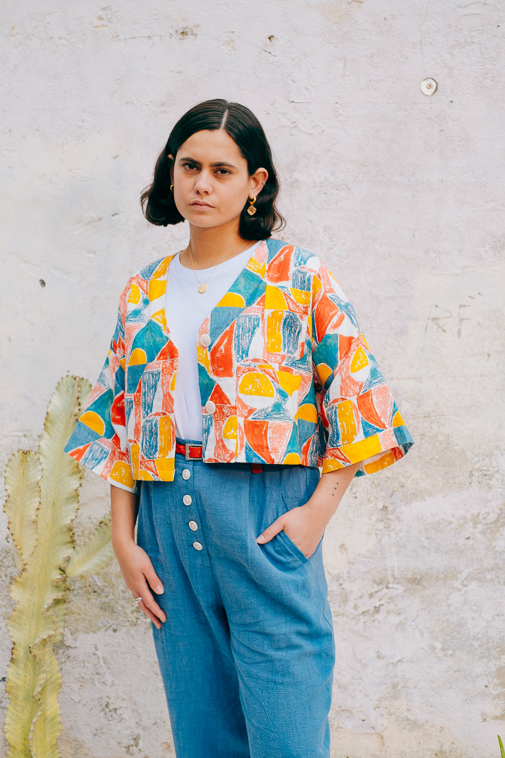A colorful geometric patterned linen jacket with a V-neckline, elbow length sleeves, and a cropped fit.
