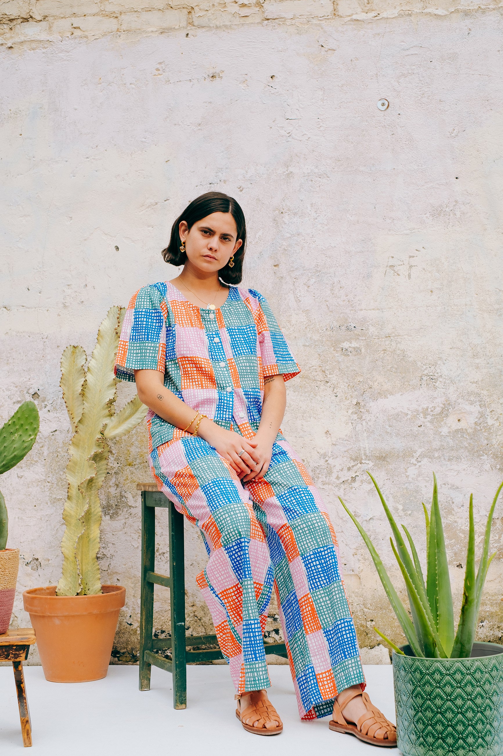 A pair of straight leg trousers with a multicolored grid check pattern. The trousers have a flat front, elasticated waist at the back, and side patch pockets.