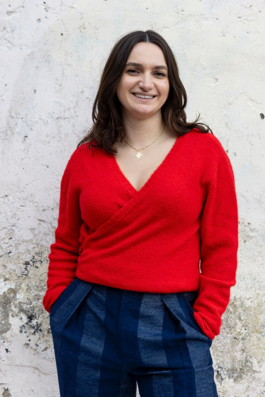 Woman wearing a red sweater and blue plaid pants against a textured white wall.