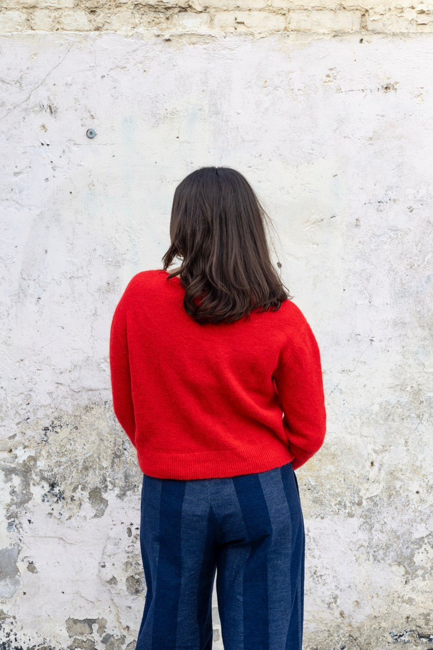 Person wearing a red sweater and blue pants standing against a textured white wall.