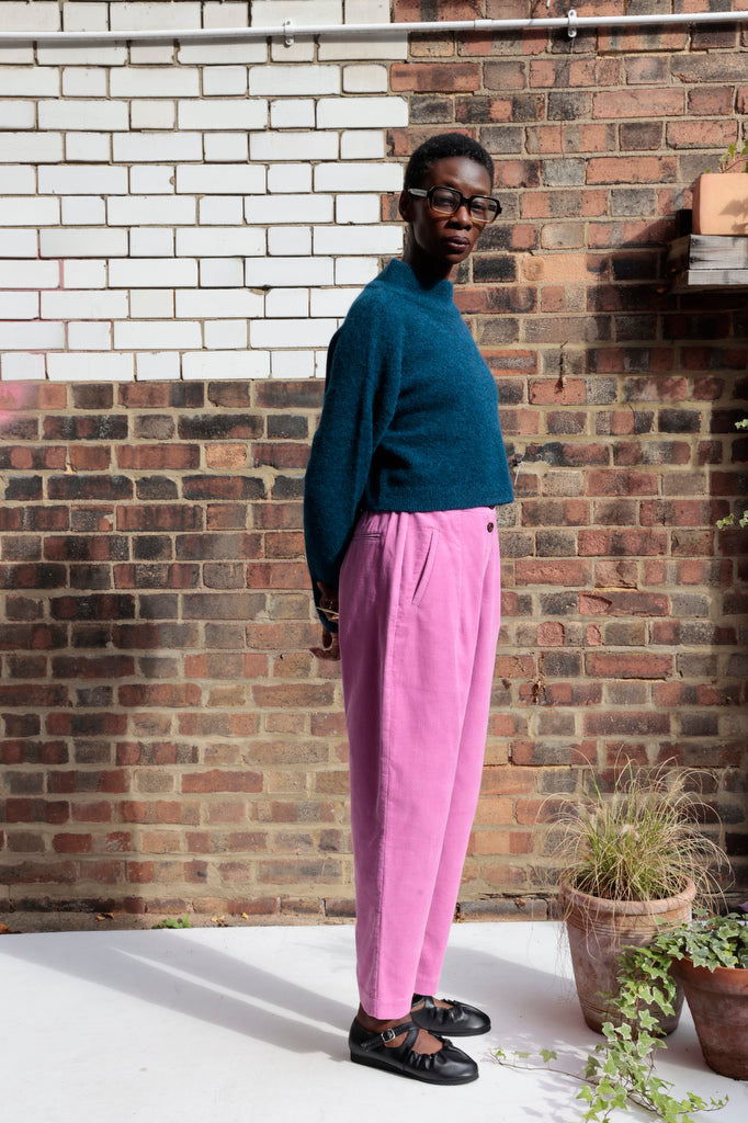 Person wearing a teal sweater and pink pants standing against a brick wall.