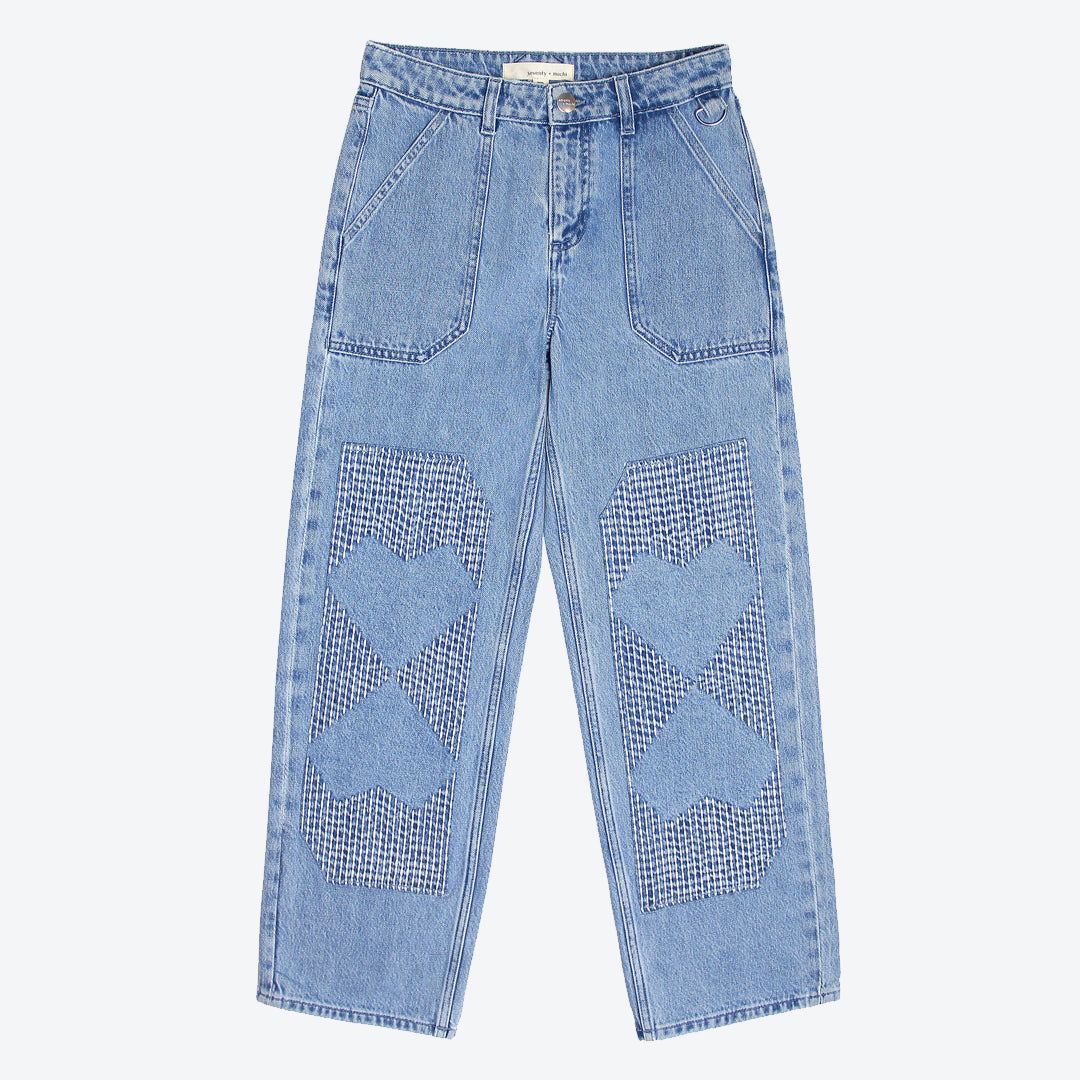 A pair of straight-leg blue jeans with carpenter style patches and embroidery stitches in the shape of hearts on the front legs.