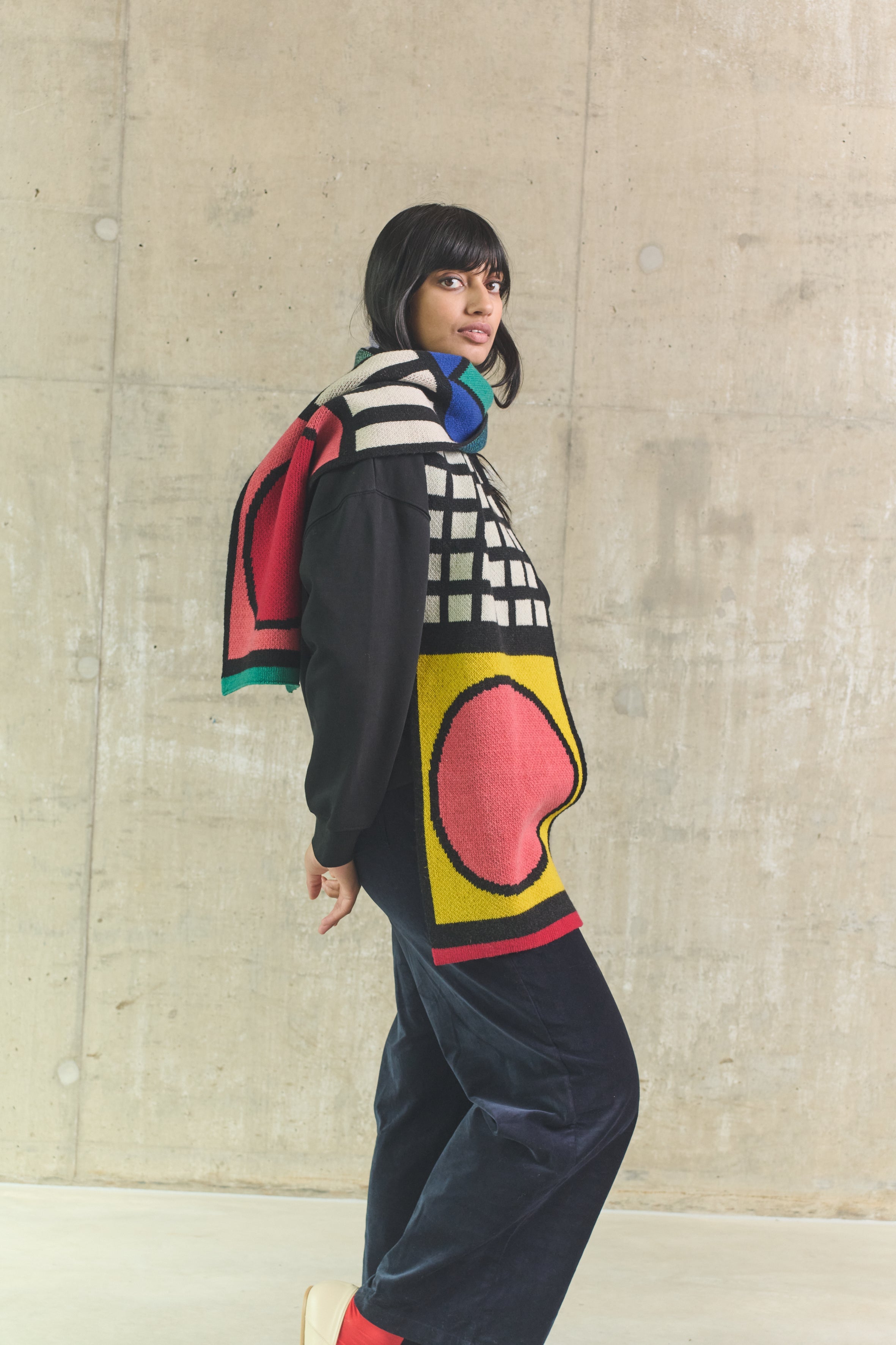 Person wearing a colorful sweater with abstract patterns against a concrete wall.
