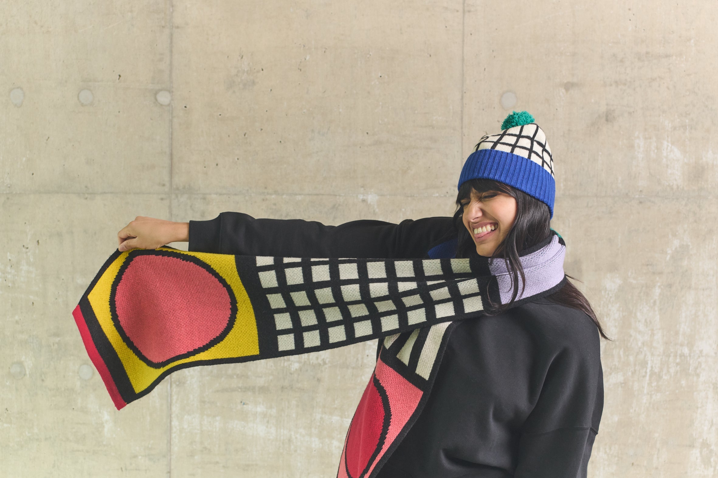 Person wearing a colorful scarf and beanie against a concrete wall