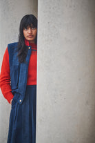 Person wearing a red sweater and blue vest against a gray wall