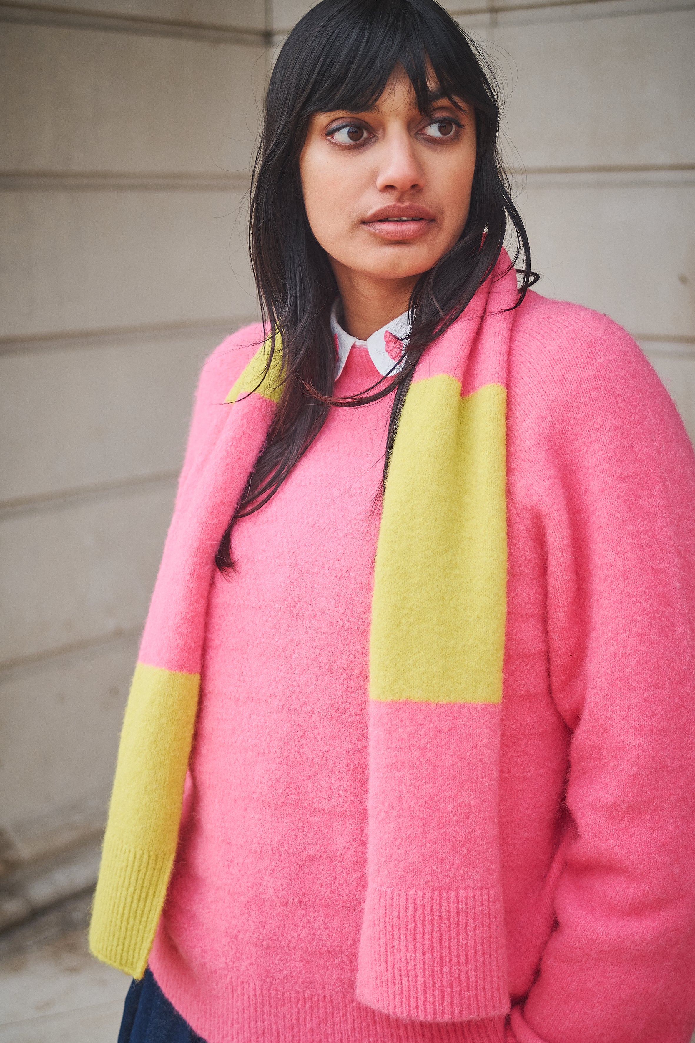 Person wearing a pink sweater with a yellow scarf against a neutral background