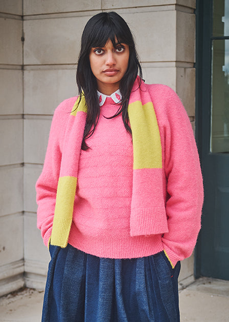 Person wearing a pink sweater with a yellow scarf in an urban setting